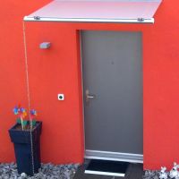 Filigran Vordach an roter Fassade mit Milchglas. 